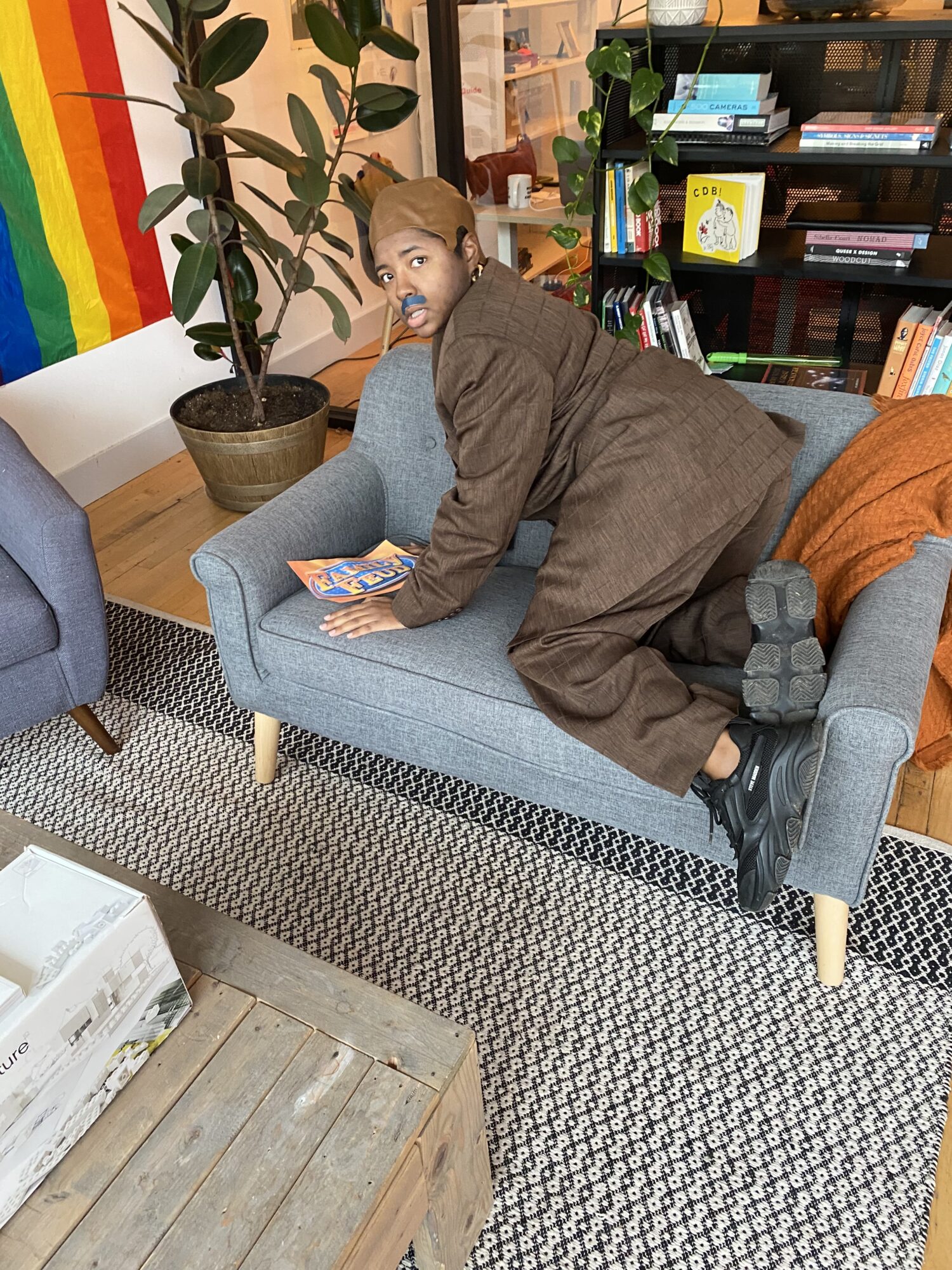Raven as Steve Harvey sits on all fours on a couch and looks frightened at the photographer